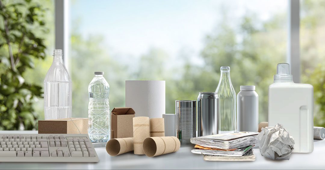Diez objetos reciclables sobre una mesa blanca iluminada: papel, cartón, plásticos, metales, vidrio, Tetra Pak y RAEE
